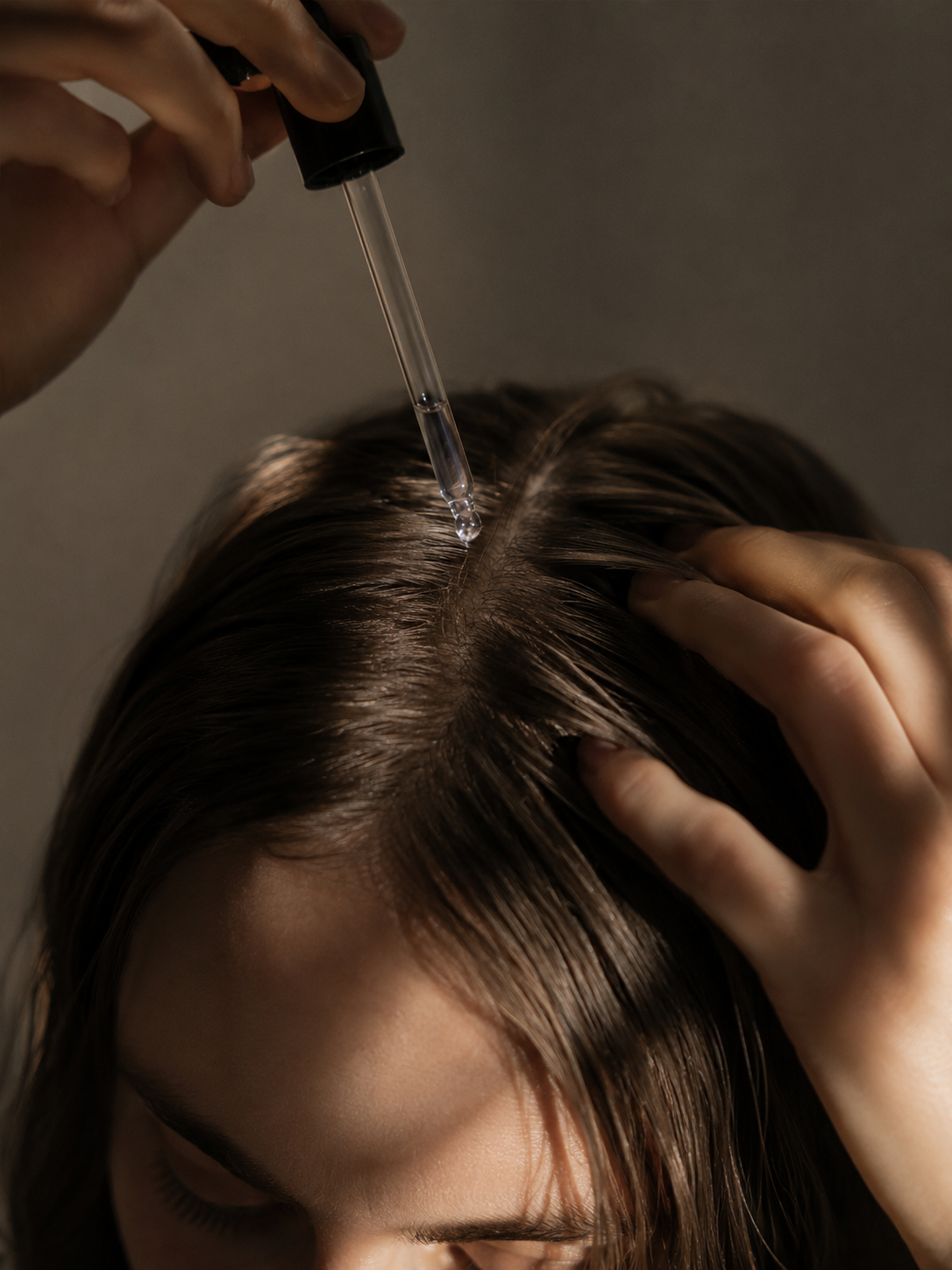 Editorial close-up of castor oil being applied to the scalp with a glass dropper in warm cinematic light.