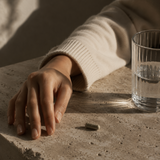 “Minimal editorial close-up of a herbal capsule beside a glass of water on stone surface representing a daily wellness ritual.”