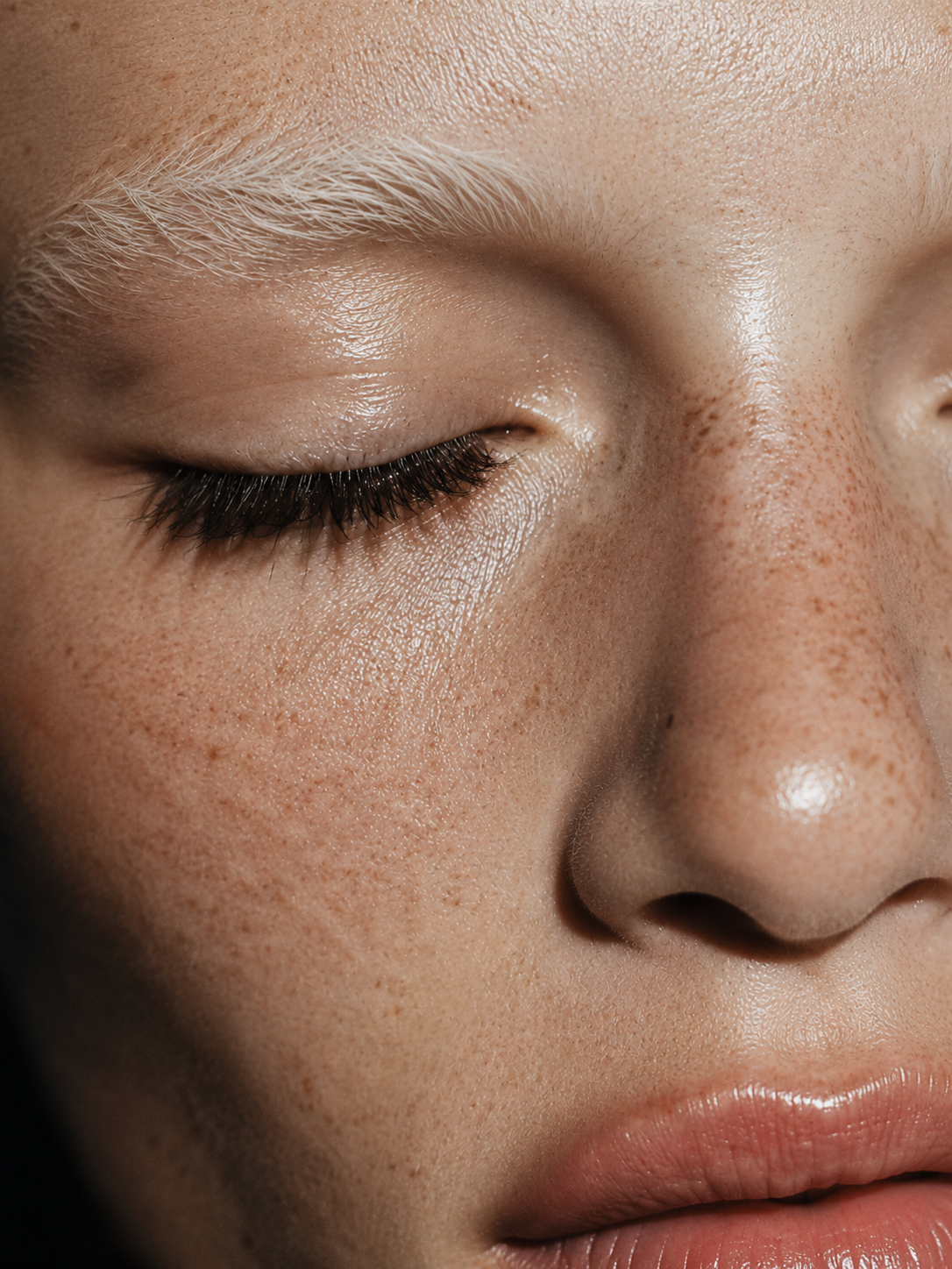 Nahaufnahme einer Gesichtshaut mit natürlicher Hautstruktur, Sommersprossen und langen Wimpern.